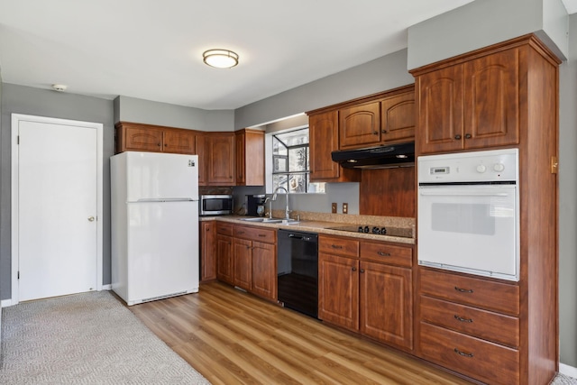 kitchen with light wood-style floors, under cabinet range hood, light countertops, black appliances, and a sink