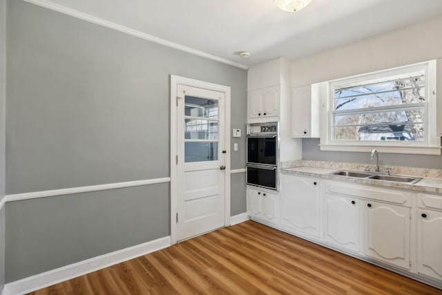 kitchen with light wood-style flooring, oven, a sink, white cabinetry, and a warming drawer