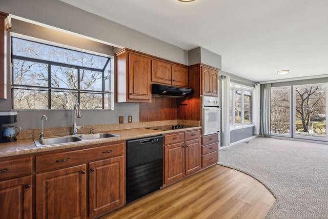 kitchen featuring light countertops, light wood-style flooring, a sink, under cabinet range hood, and black appliances