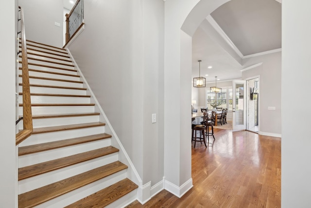 stairs with crown molding, baseboards, arched walkways, and wood finished floors