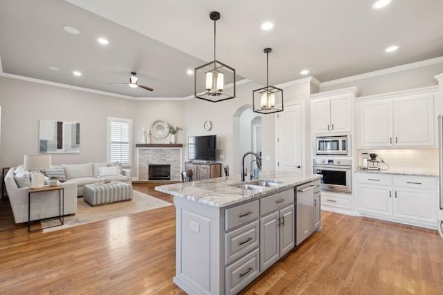 kitchen featuring arched walkways, white cabinets, an island with sink, stainless steel appliances, and gray cabinetry