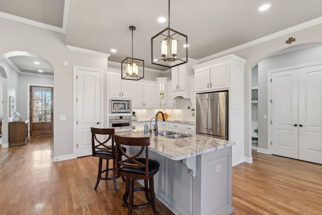 kitchen with appliances with stainless steel finishes, arched walkways, a sink, and wood finished floors