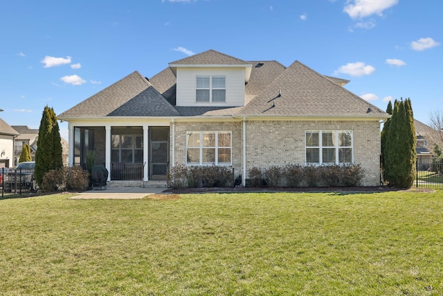 rear view of property with a sunroom, brick siding, a yard, and fence