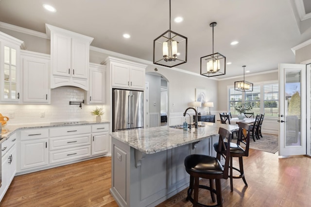 kitchen featuring arched walkways, black electric stovetop, light wood finished floors, high end fridge, and a sink