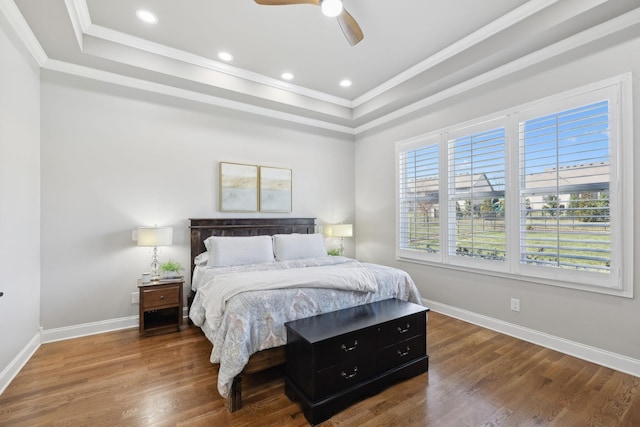 bedroom featuring baseboards, wood finished floors, a raised ceiling, and crown molding