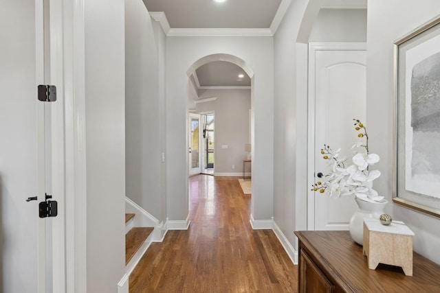 hallway featuring baseboards, arched walkways, dark wood finished floors, and crown molding