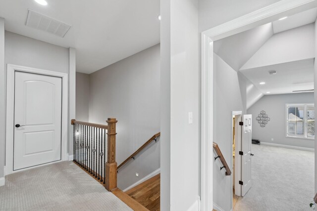 hallway with carpet floors, visible vents, vaulted ceiling, an upstairs landing, and baseboards