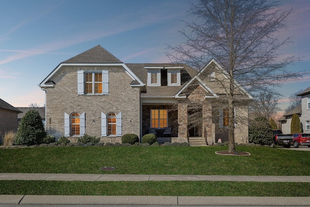 view of front facade with a front yard, brick siding, and roof with shingles