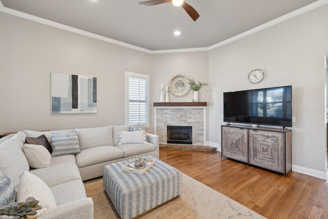 living area with baseboards, ceiling fan, wood finished floors, crown molding, and a brick fireplace