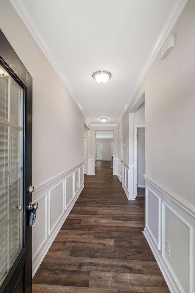 corridor with crown molding, dark wood finished floors, a wainscoted wall, and a decorative wall