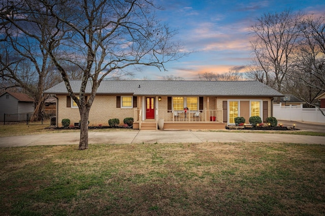 single story home featuring covered porch, brick siding, a shingled roof, fence, and a lawn