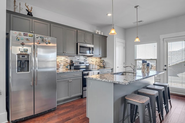 kitchen with stainless steel appliances, tasteful backsplash, gray cabinets, a sink, and light stone countertops