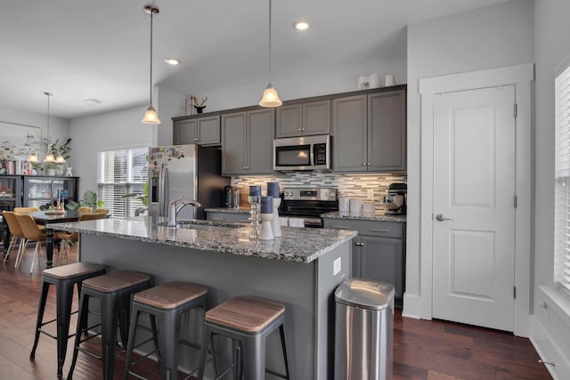 kitchen with appliances with stainless steel finishes, a sink, a breakfast bar, and gray cabinetry