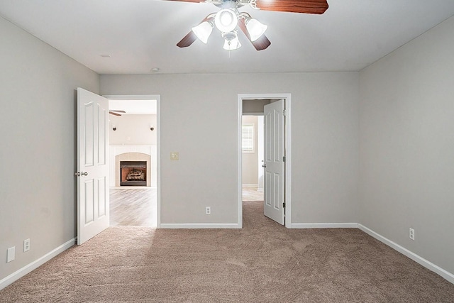 unfurnished bedroom featuring carpet floors, a fireplace with flush hearth, baseboards, and ceiling fan