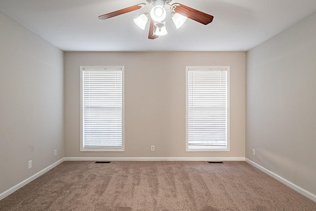 carpeted empty room featuring a healthy amount of sunlight, visible vents, and baseboards