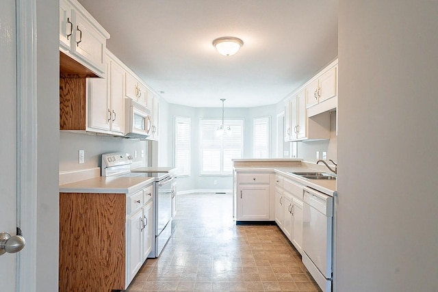 kitchen featuring white appliances, decorative light fixtures, light countertops, white cabinetry, and a sink