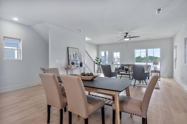 dining space featuring light wood finished floors, visible vents, a ceiling fan, baseboards, and stairs