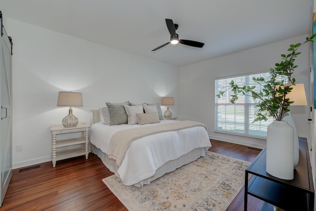 bedroom with a barn door, visible vents, and dark wood finished floors