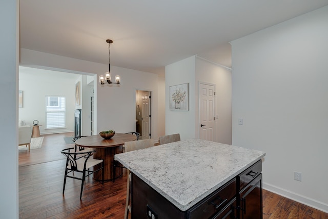 kitchen with a notable chandelier, hanging light fixtures, dark wood-type flooring, a kitchen island, and baseboards