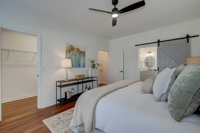 bedroom featuring a barn door, baseboards, a ceiling fan, wood finished floors, and a spacious closet