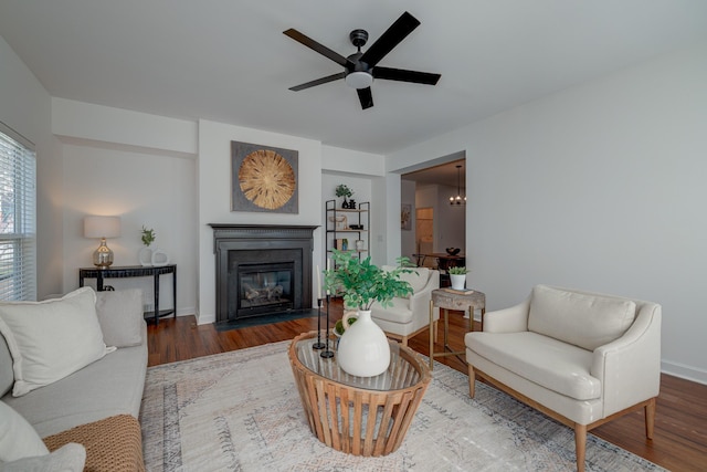 living area featuring a fireplace with flush hearth, baseboards, ceiling fan, and wood finished floors