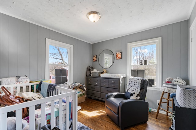 bedroom featuring a crib, ornamental molding, multiple windows, and wood finished floors