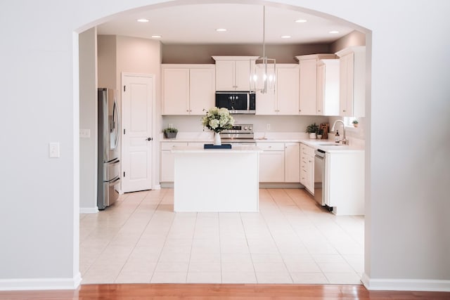 kitchen with arched walkways, white cabinets, light countertops, appliances with stainless steel finishes, and a center island