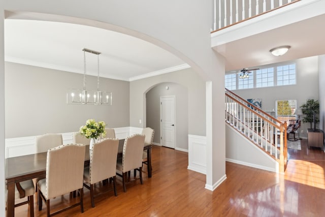 dining space with stairway, wood finished floors, arched walkways, ornamental molding, and ceiling fan with notable chandelier