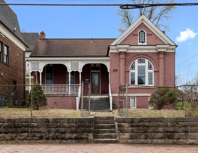 victorian-style house featuring covered porch, brick siding, and a chimney