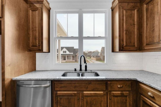 kitchen featuring tasteful backsplash, dishwasher, light stone counters, and a sink