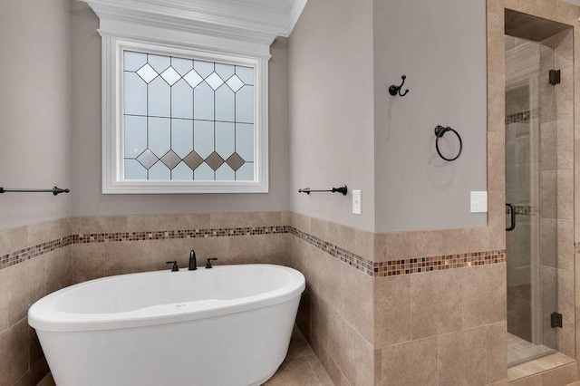 bathroom featuring ornamental molding, a soaking tub, a shower stall, and tile walls