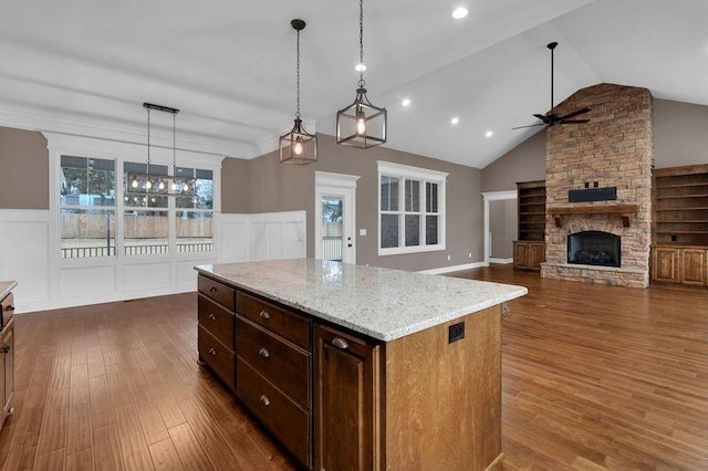 kitchen with dark wood-type flooring, a fireplace, a ceiling fan, hanging light fixtures, and light stone countertops