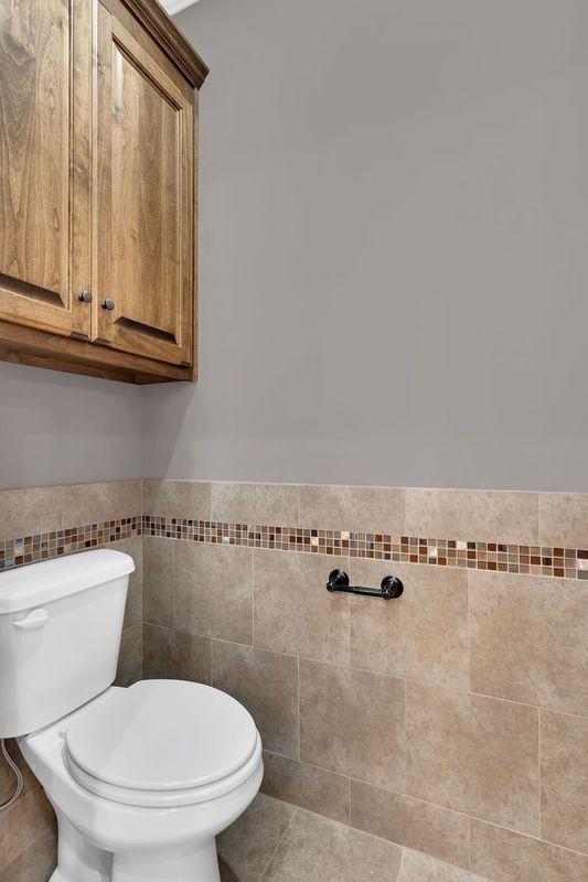 bathroom featuring a wainscoted wall, tile walls, toilet, and tile patterned floors