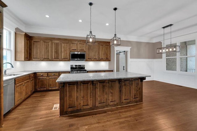 kitchen with appliances with stainless steel finishes, ornamental molding, dark wood-type flooring, a center island, and a sink