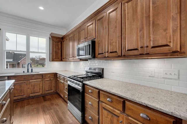 kitchen with brown cabinets, decorative backsplash, appliances with stainless steel finishes, ornamental molding, and a sink