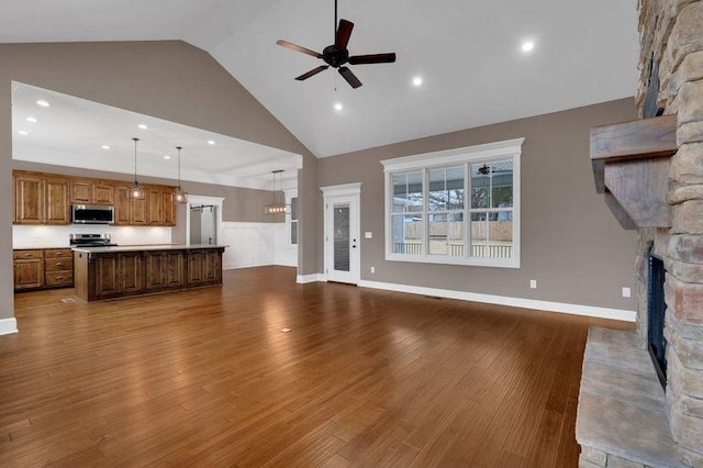 unfurnished living room with a ceiling fan, a stone fireplace, wood finished floors, high vaulted ceiling, and baseboards