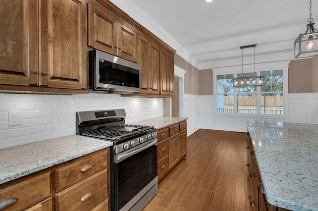 kitchen featuring stainless steel appliances, ornamental molding, light stone countertops, dark wood-style floors, and decorative light fixtures