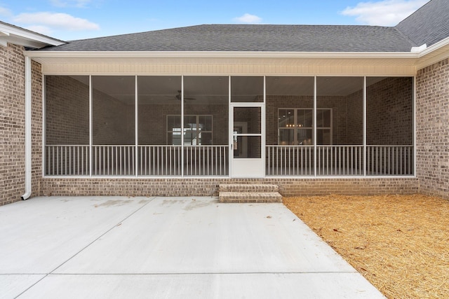 property entrance featuring a shingled roof, a patio, and brick siding