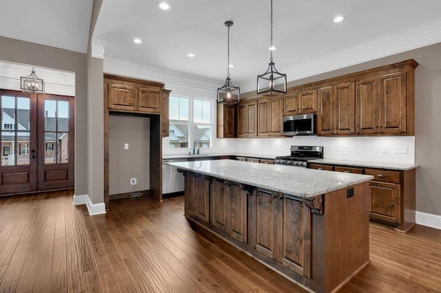 kitchen with ornamental molding, dark wood-style flooring, a center island, stainless steel appliances, and backsplash