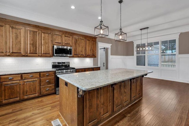 kitchen with a kitchen island, wood finished floors, visible vents, appliances with stainless steel finishes, and light stone countertops