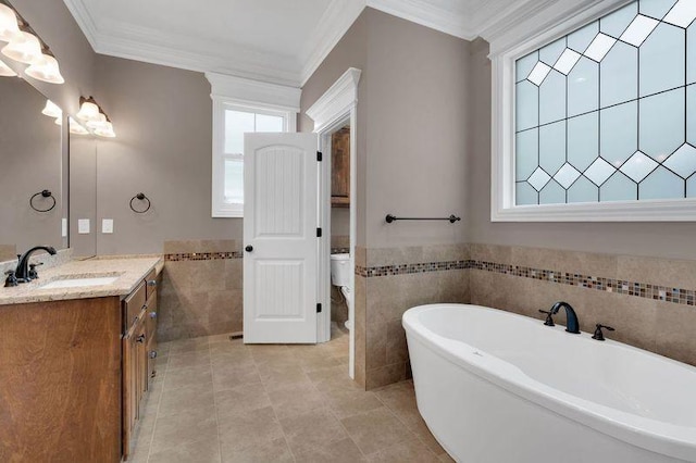 bathroom with toilet, ornamental molding, vanity, a freestanding tub, and tile walls