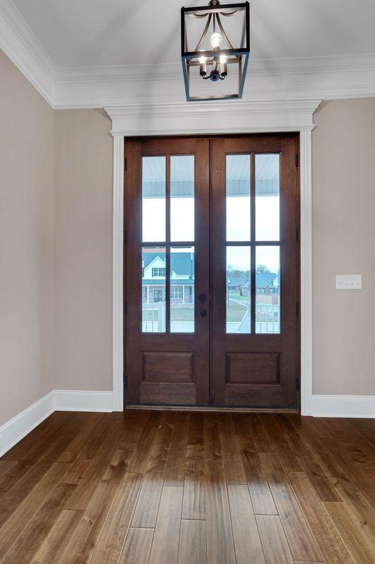 doorway featuring a chandelier, wood finished floors, baseboards, french doors, and crown molding