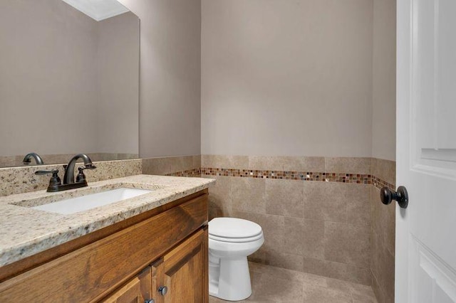 bathroom with toilet, a wainscoted wall, tile patterned flooring, vanity, and tile walls