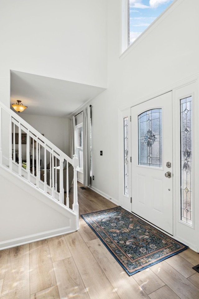 entrance foyer featuring stairs, a towering ceiling, baseboards, and wood finished floors