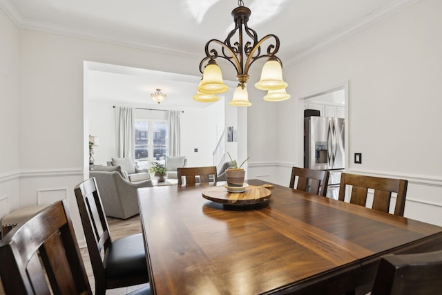 dining room featuring crown molding, wainscoting, light wood-type flooring, and an inviting chandelier