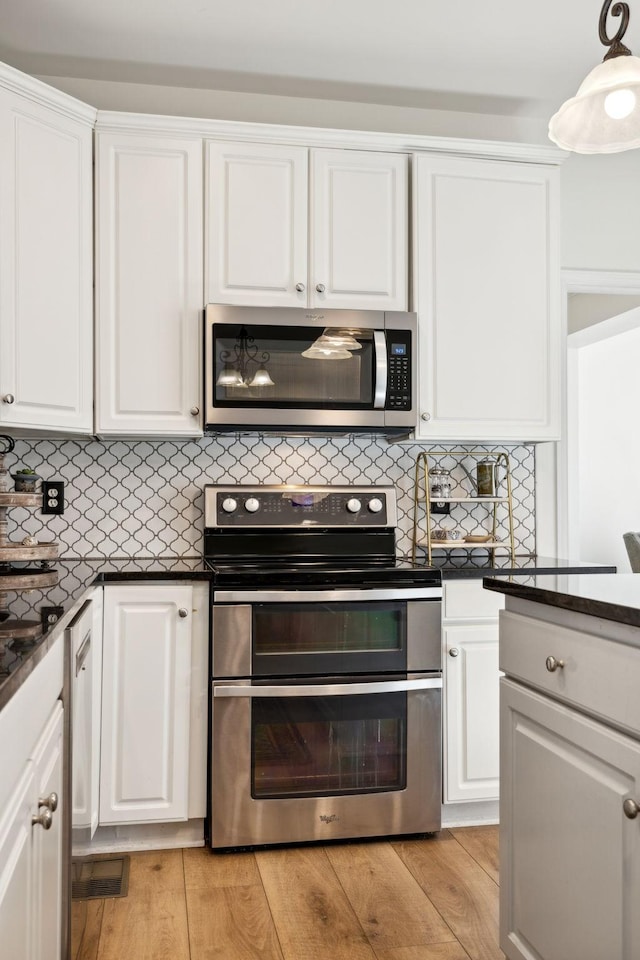 kitchen featuring appliances with stainless steel finishes, dark countertops, white cabinetry, and light wood-style floors