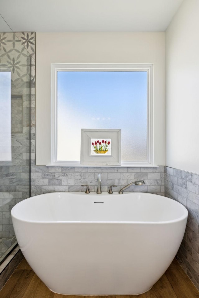 bathroom featuring a soaking tub, plenty of natural light, tile walls, and wood finished floors