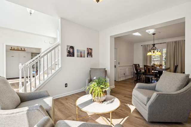 living area with baseboards, wood finished floors, an inviting chandelier, stairs, and crown molding