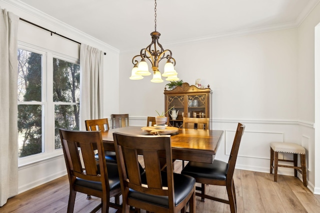 dining area with light wood-style flooring, ornamental molding, a notable chandelier, and wainscoting