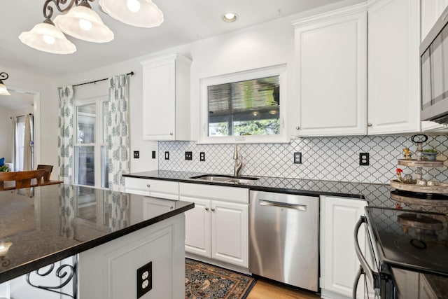 kitchen with decorative backsplash, white cabinets, appliances with stainless steel finishes, dark stone countertops, and a sink